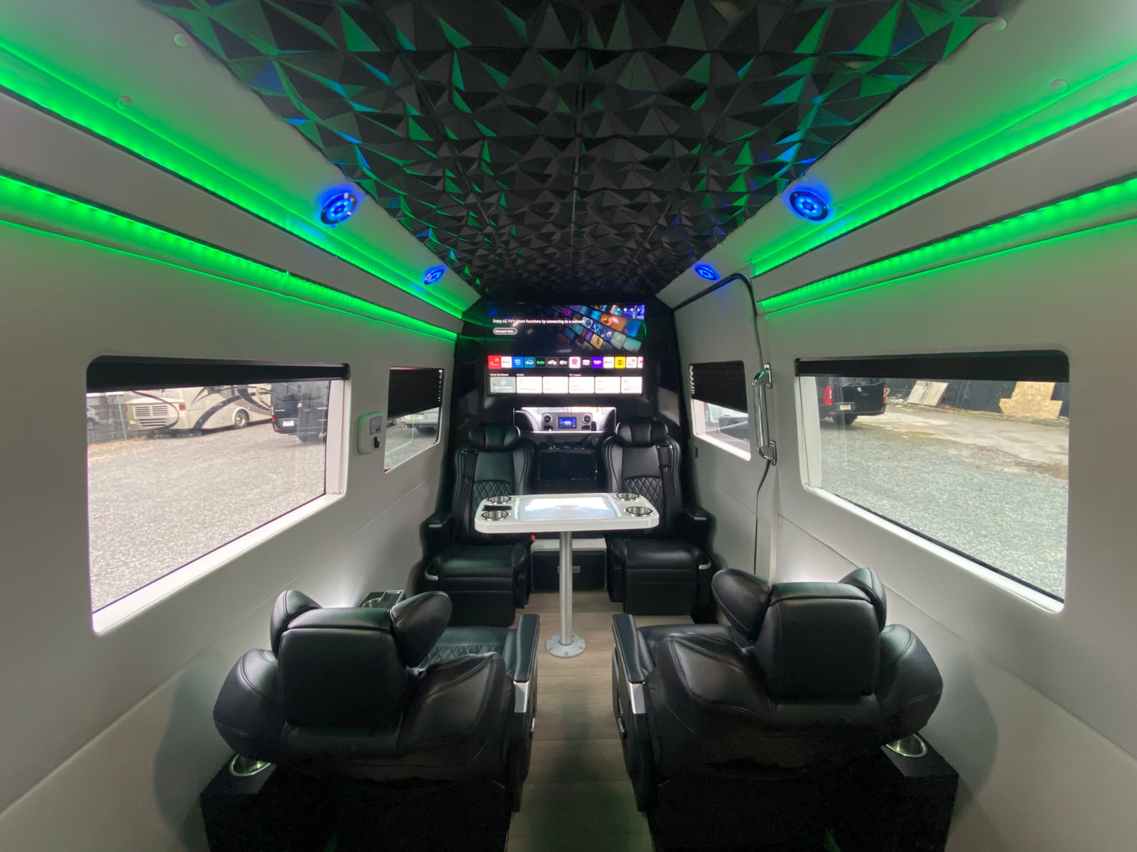 Spacious rv rental interior featuring ambient green LED lighting, a geometric ceiling, plush black seating, and a large entertainment screen.