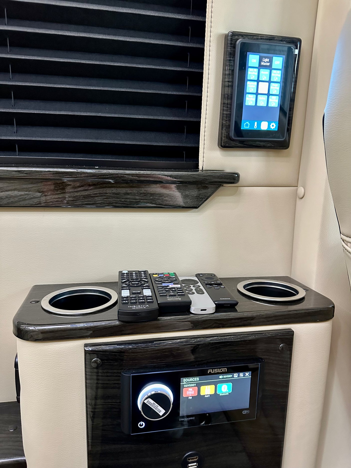 Inside an RV rental: control panel for lights, Fusion audio system, remotes, and cupholders for a comfortable journey.