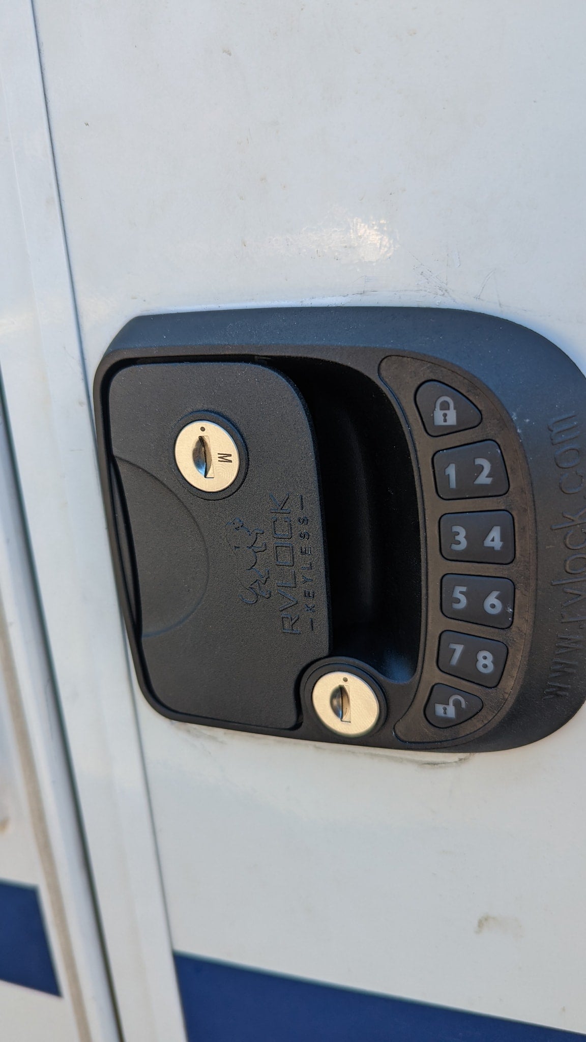 Close-up of an RV rental door with a black digital keypad entry lock, featuring keyholes and numerical buttons for keyless access.