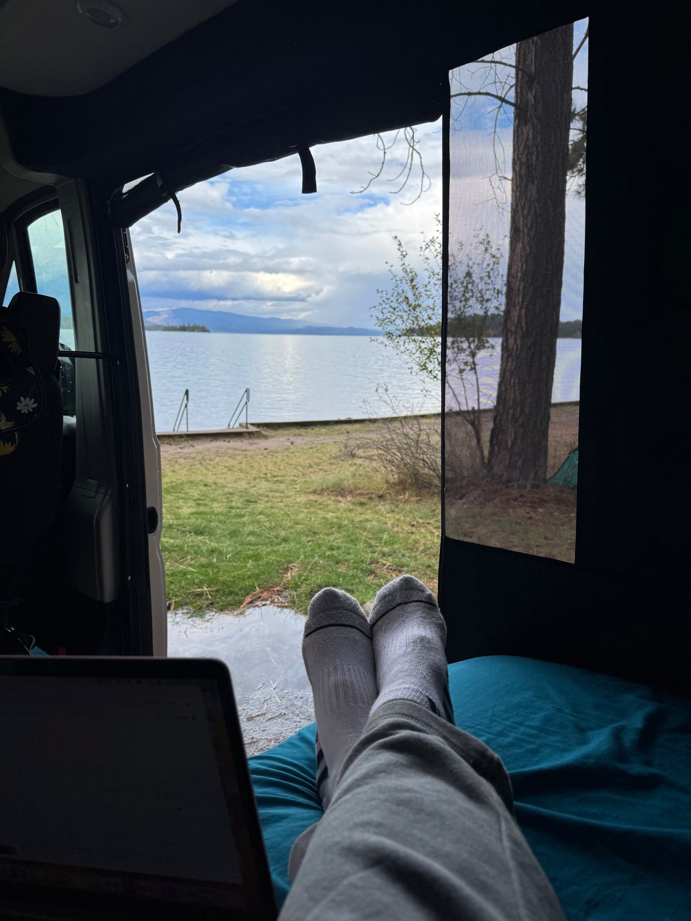 Feet up in a comfy rv rental, laptop open, enjoying a beautiful lake view through the screen door.