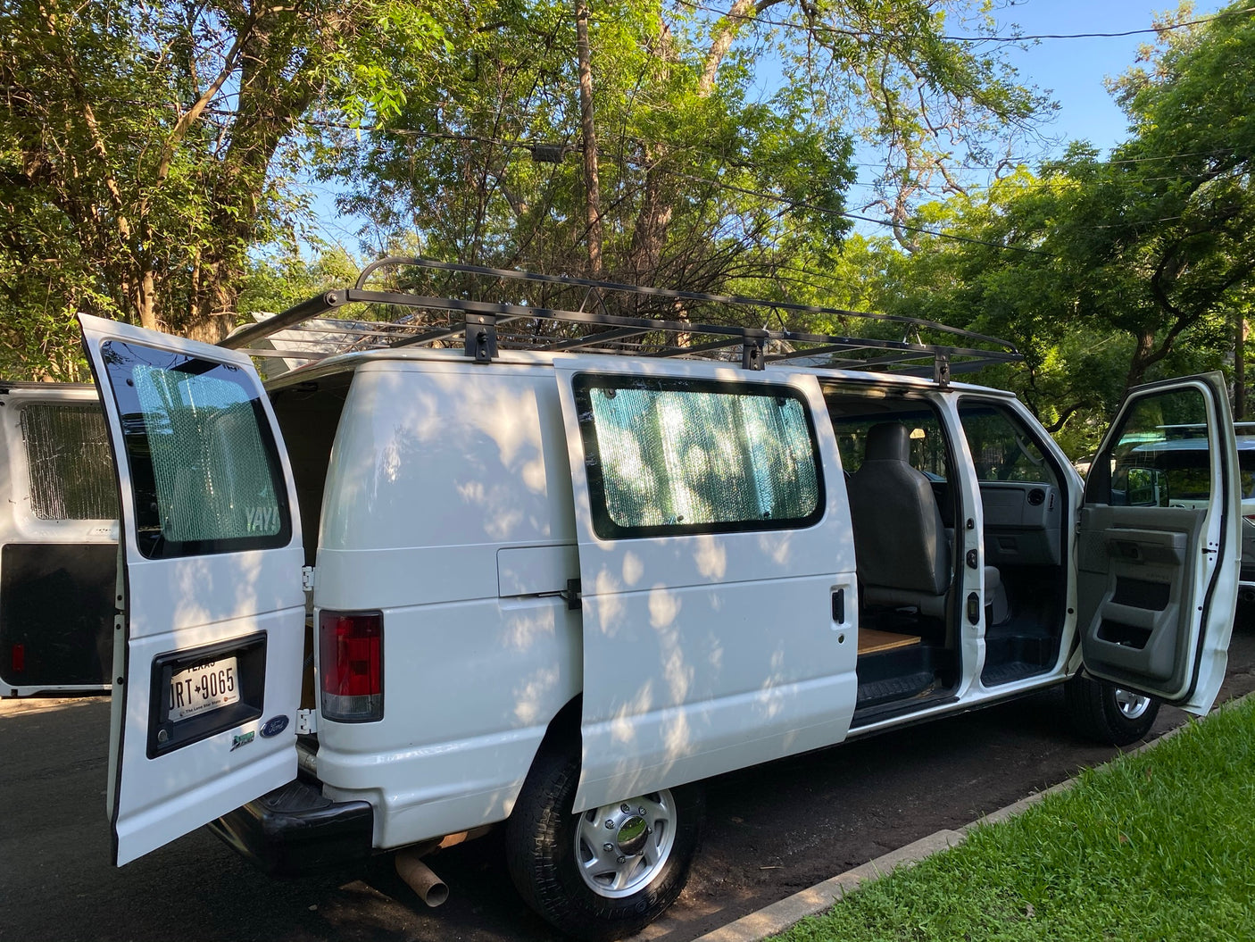 doors open & roof rack. Parked curbside under trees.|Explore big landscapes! This white camper van