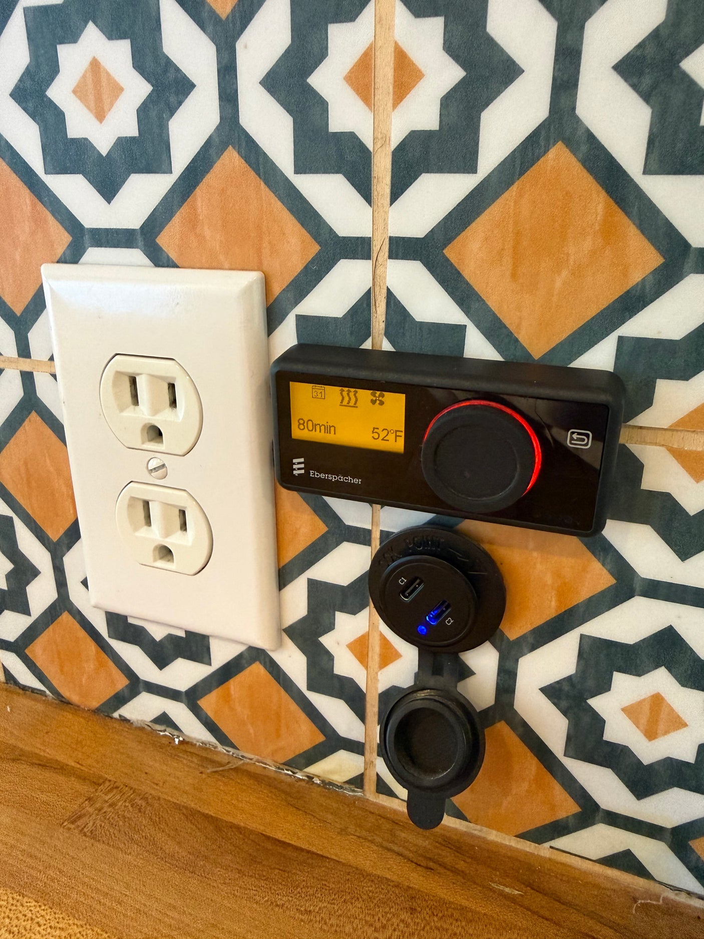 RV rental amenities: Wall outlet, Eberspächer climate control (52°F, 80min runtime), and dual USB charger on patterned tiles.