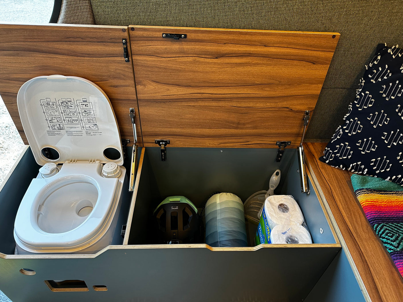 Inside an **rv rental**: a portable toilet and clever storage for camping gear like a sleeping bag & toilet paper.