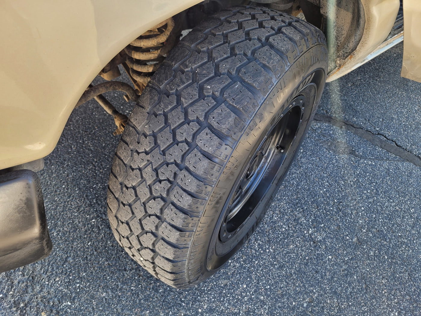 Close-up of an RV rental's front wheel, showcasing its rugged tire tread and visible suspension on asphalt. — photo 4