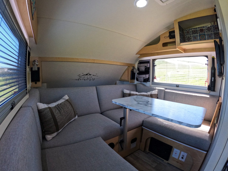 Cozy RV rental interior: U-shaped dinette, marble-top table, "Life is for adventure" decal, perfect for travel and comfort.