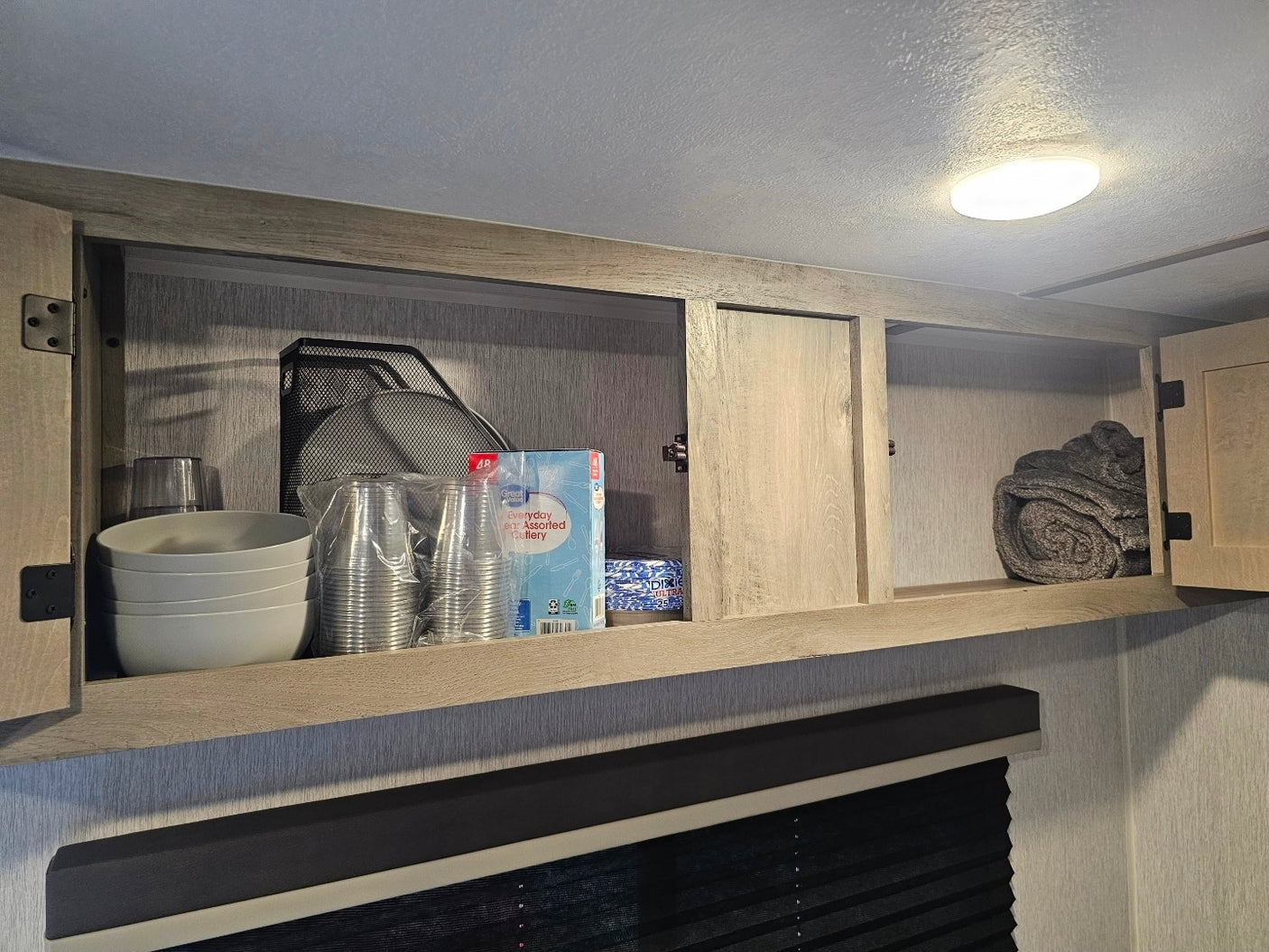 Inside an RV rental cabinet: organized kitchenware like bowls, cups, cutlery, and a neatly rolled towel.
