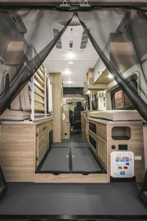 and overhead storage for road trips.|Your ultimate mobile office awaits! See a woman working in an RV rental camper van parked in a serene forest.|Spacious camper van rental interior from rear