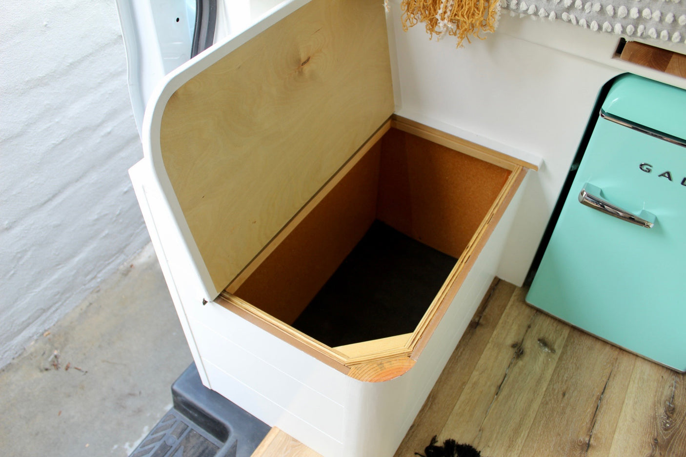 Clever storage in an RV rental! Open bench with natural wood lining, perfect for gear. Turquoise fridge nearby.