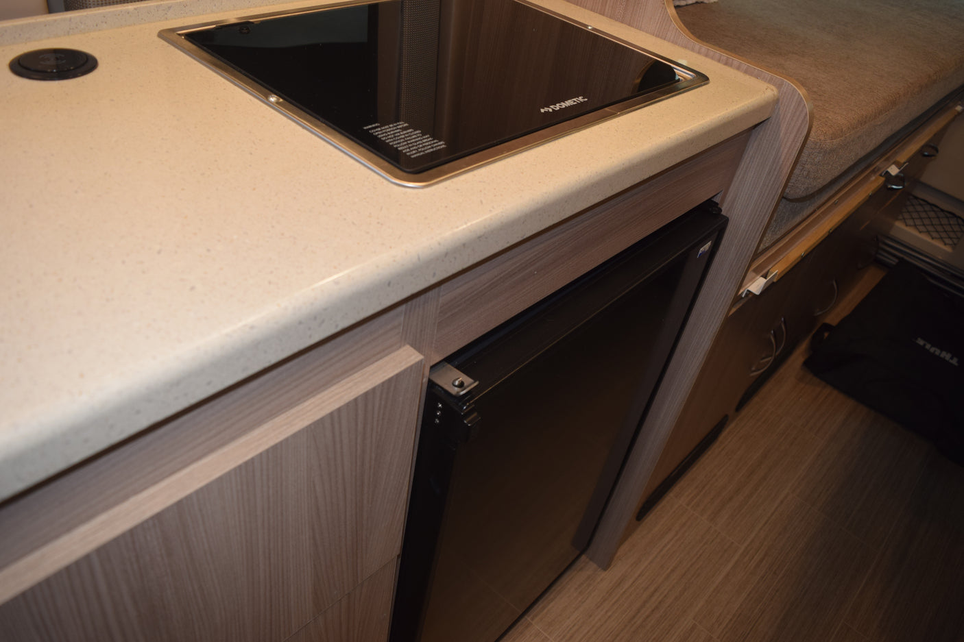 Inside an RV rental: a modern kitchen area featuring a Dometic induction cooktop, compact refrigerator, and light countertop.