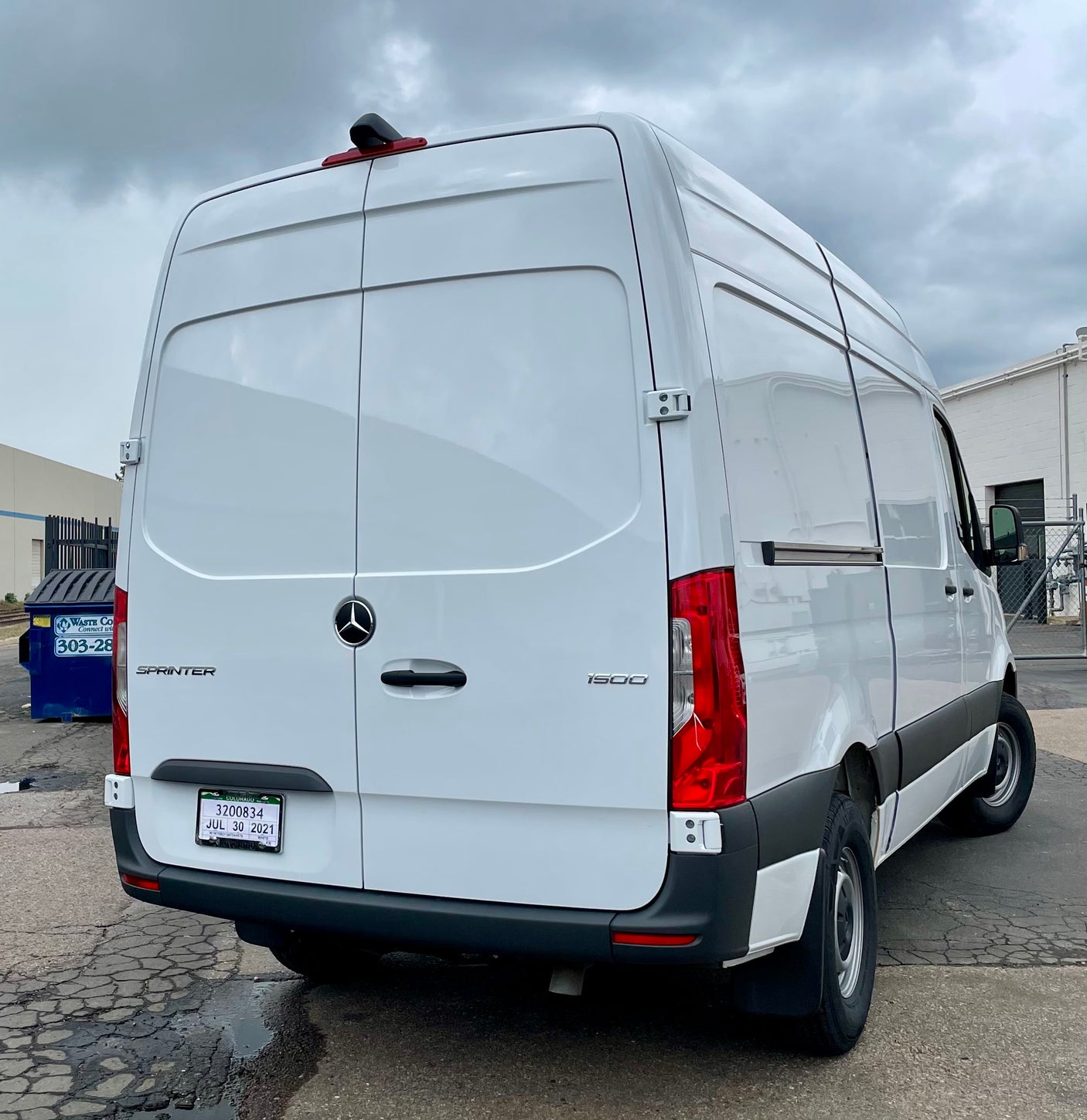 Rear view of a white Mercedes-Benz Sprinter van, suitable for an RV rental, parked on asphalt under cloudy skies.