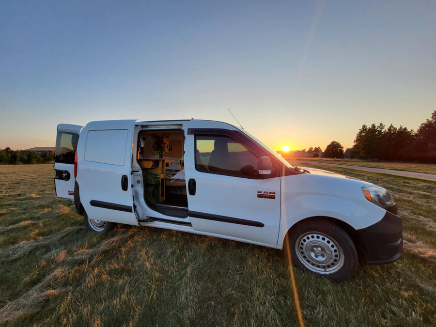 A white campervan with open doors sits in a grassy field at sunset