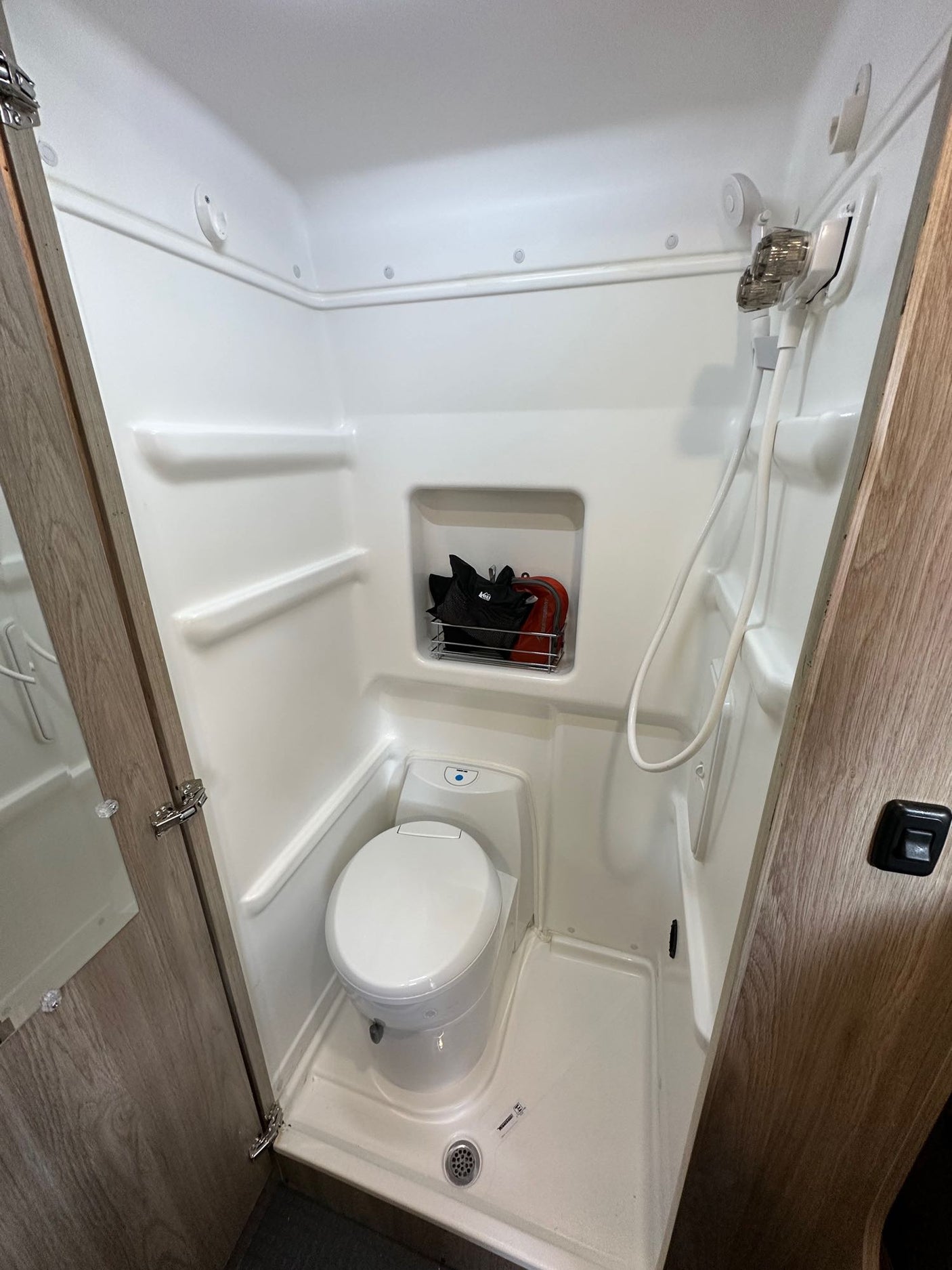 Clean and compact RV rental bathroom, featuring a white shower unit, toilet, and built-in storage.