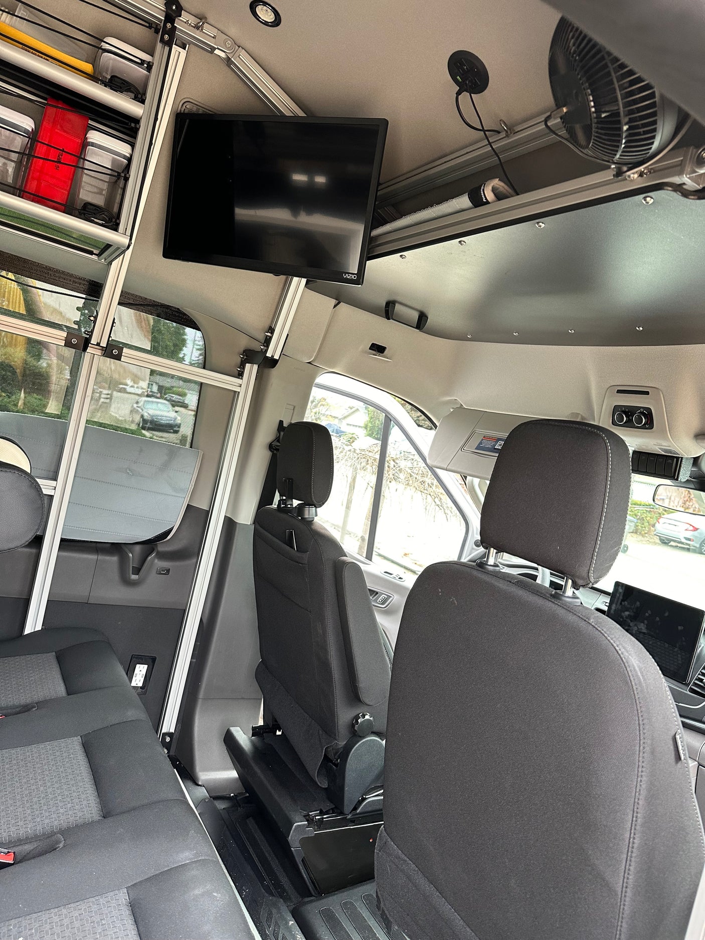 RV rental: Inside a camper van with custom aluminum shelving, a TV, fan, power outlets, and passenger seating.
