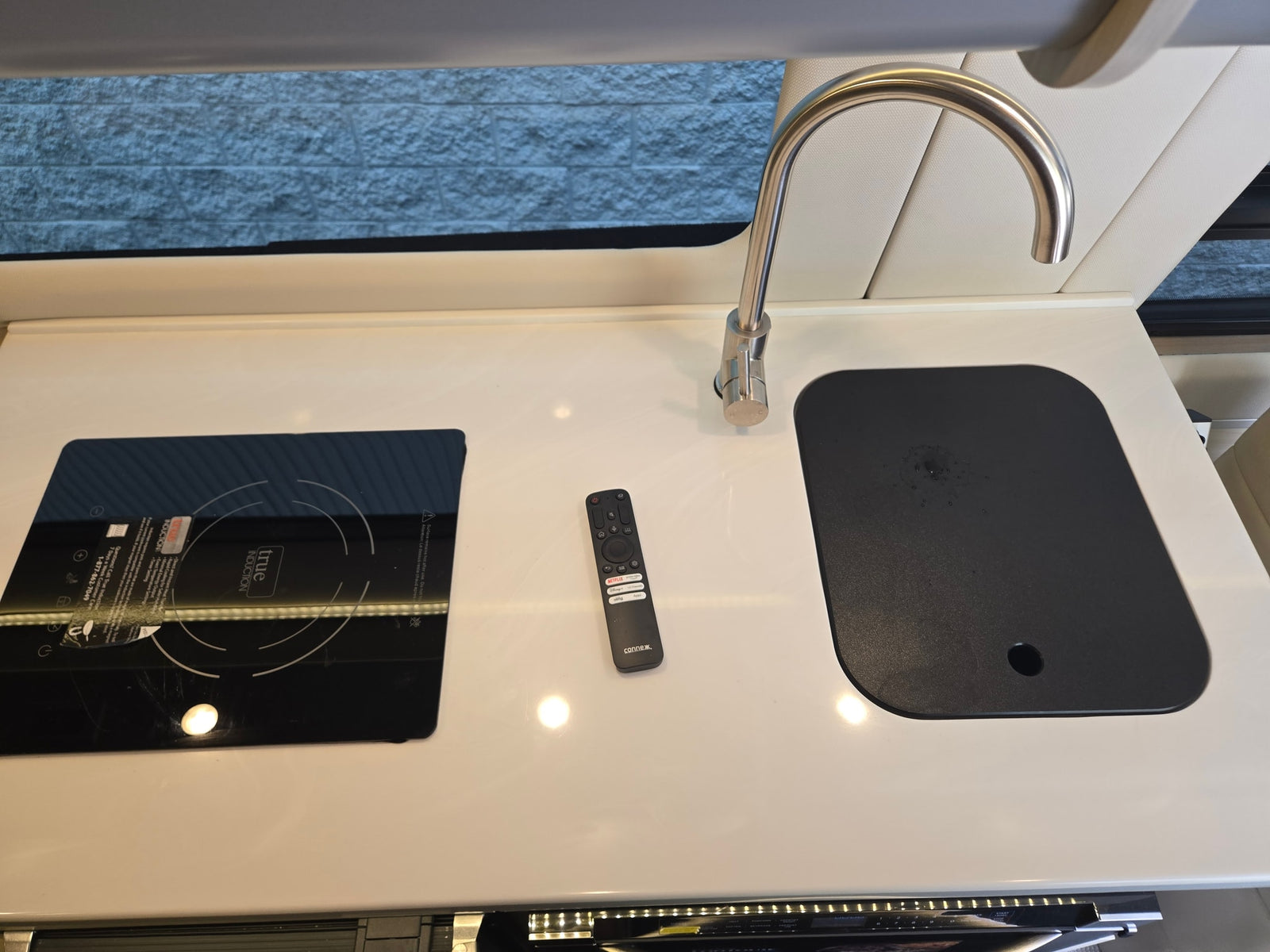 RV rental kitchen: modern induction cooktop, sink, faucet, and TV remote on a clean white countertop.