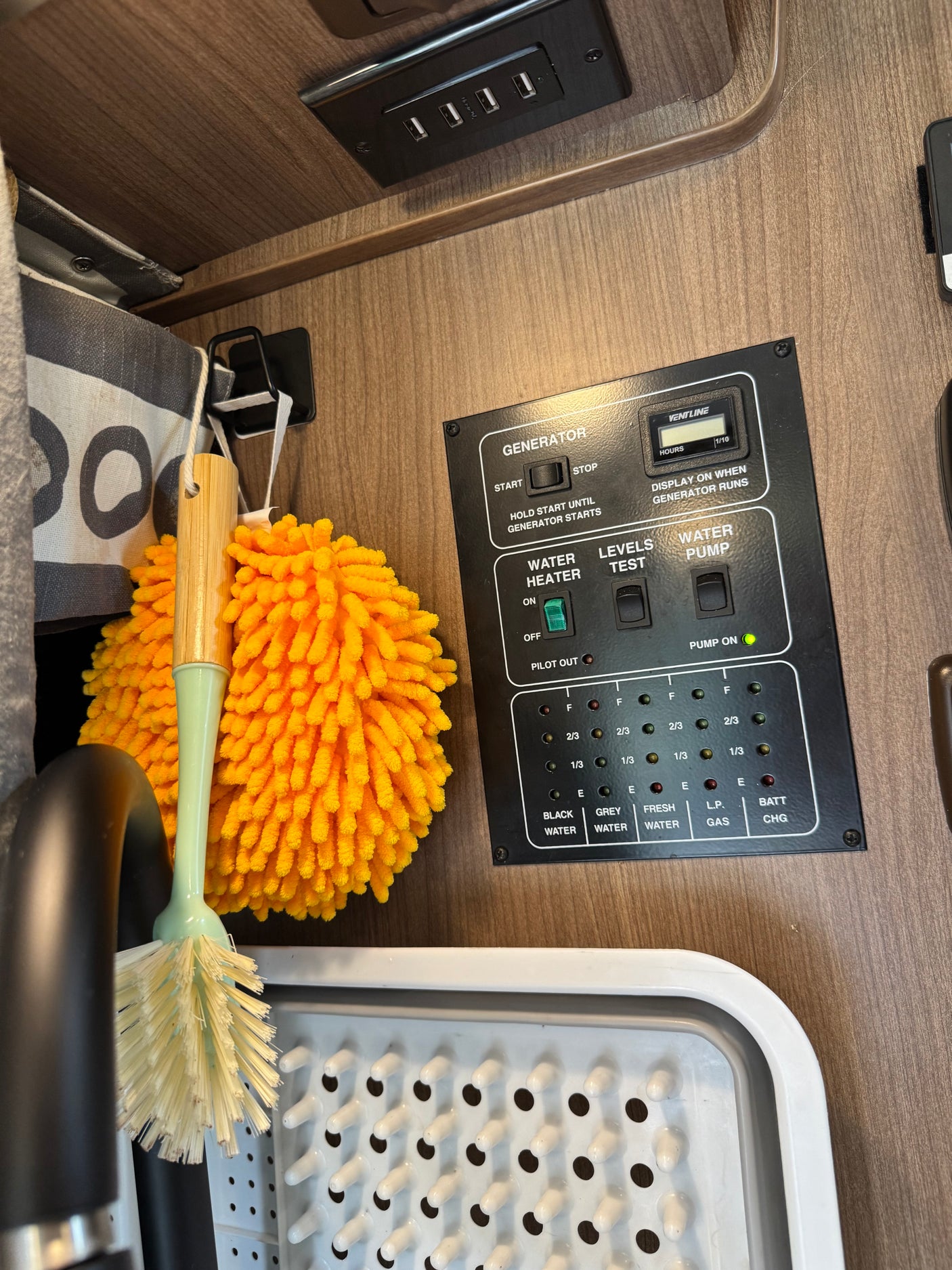 RV rental: Interior shot of a camper's control panel (generator, water levels), USB charger, dish brushes, and drainer.