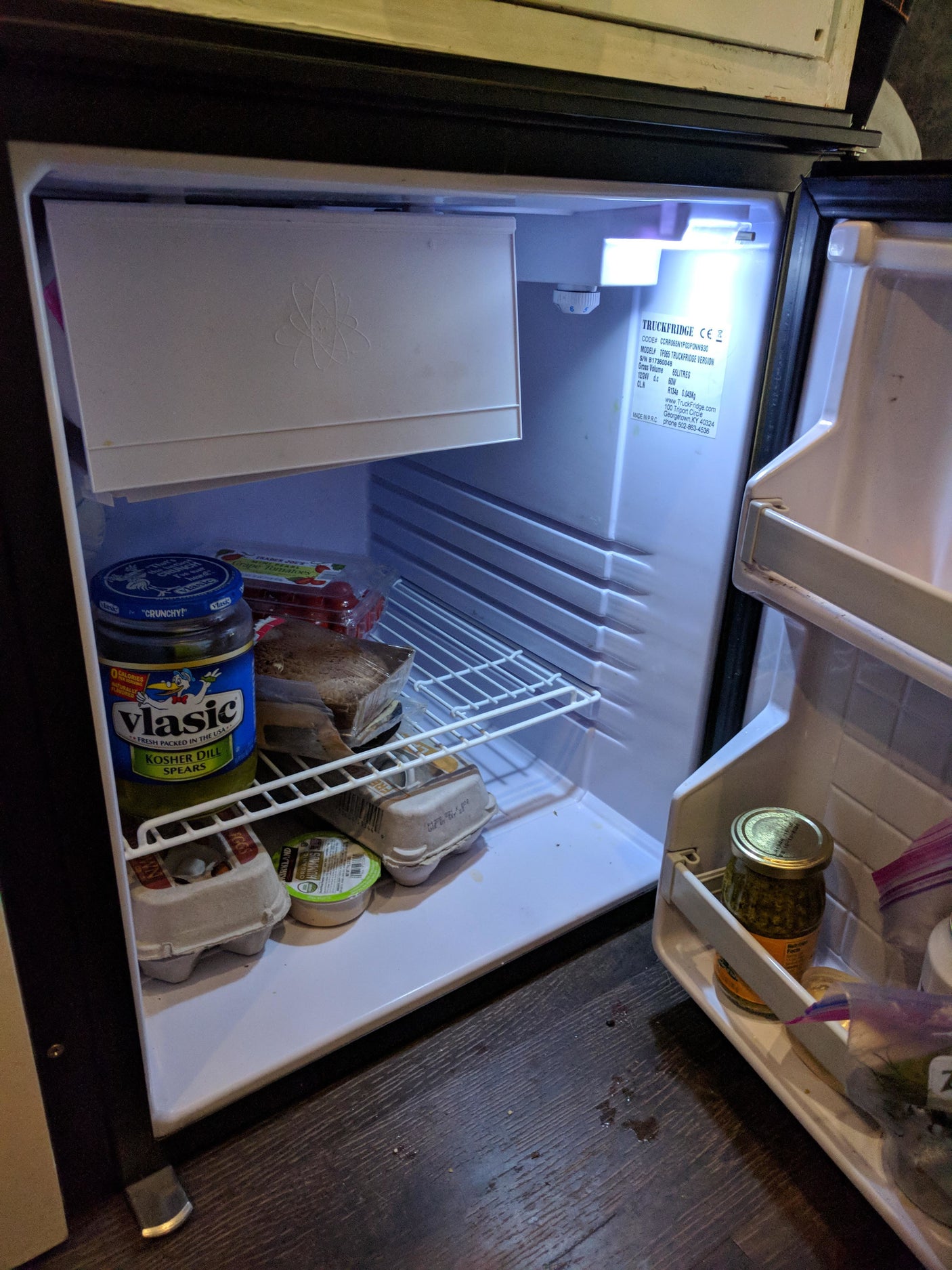 Compact fridge in an RV rental, stocked with Vlasic pickles, eggs, hummus, and tomatoes, ideal for food storage on the road.