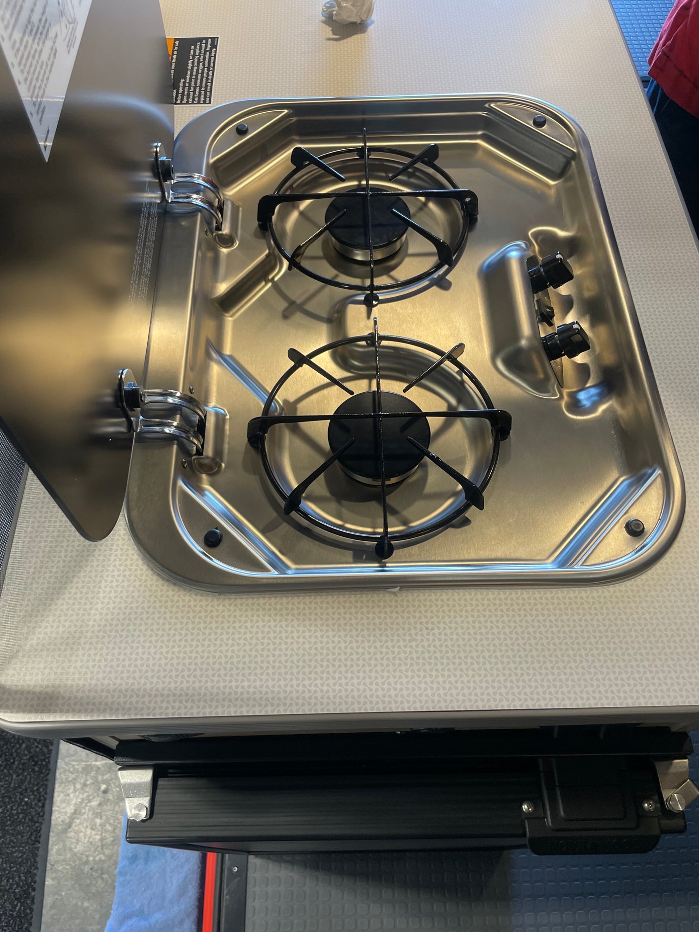 RV rental: A stainless steel, two-burner RV stove with its protective lid open, revealing black grates and control knobs.