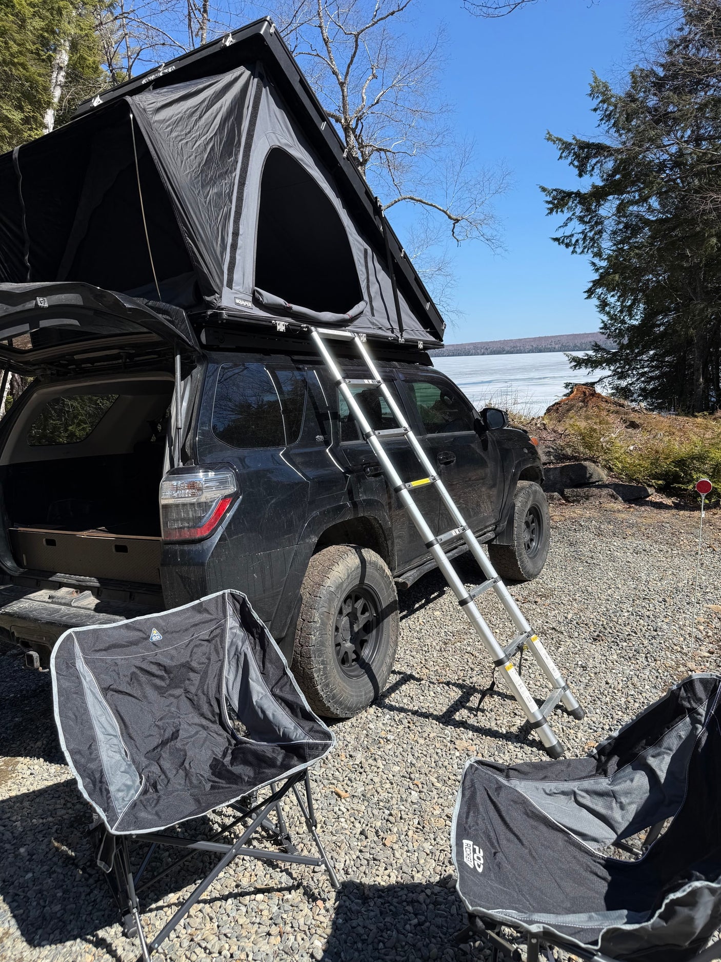 Black SUV with a deployed roof top tent by a frozen lake, ideal for an RV rental camping getaway in nature.