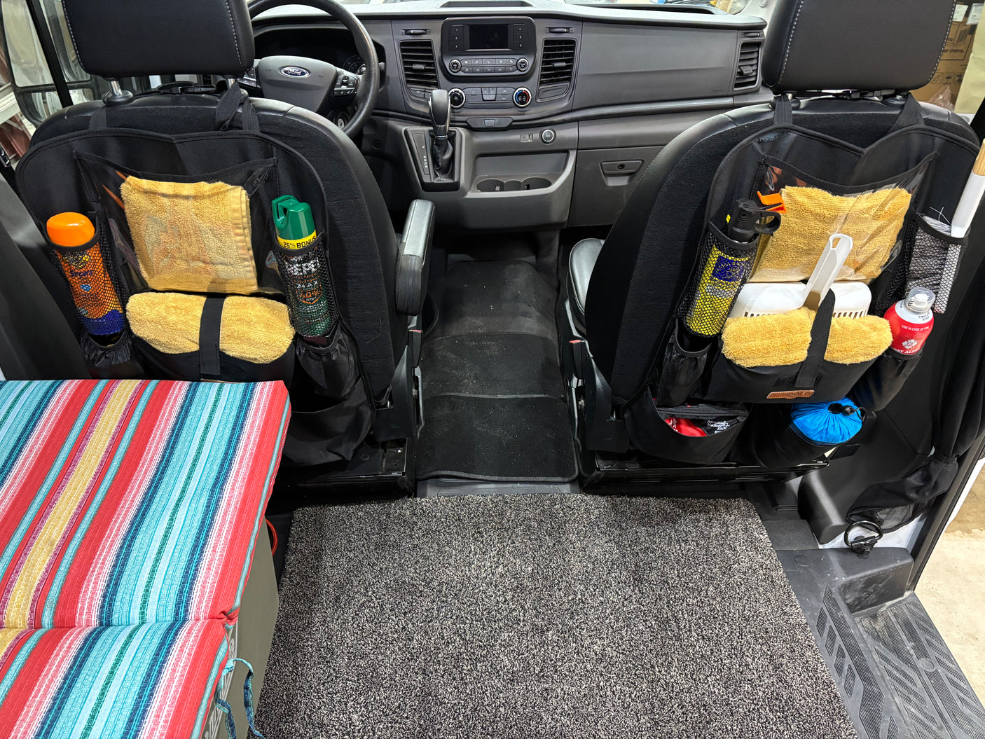 Inside an **RV rental**: front seats feature organized storage for travel gear, with a striped bed & clean floor.