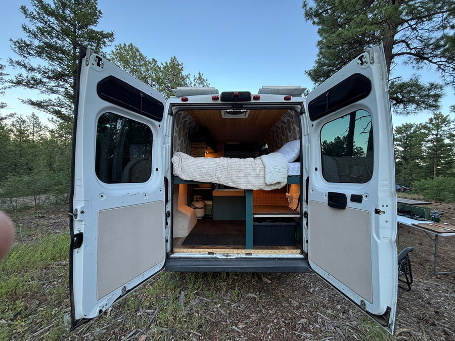 Ultimate RV rental: Customized camper van with open doors, comfy bed, solar panels, and outdoor camping setup.