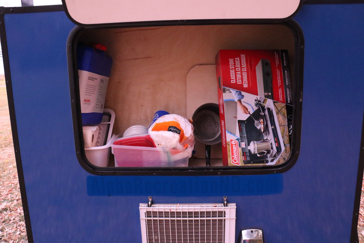 is ideal for an RV rental adventure.|This blue compact teardrop RV rental is ready for adventure! Parked on autumn leaves with its rear storage hatch open.|Compact RV rental galley showing organized camping essentials: Coleman stove