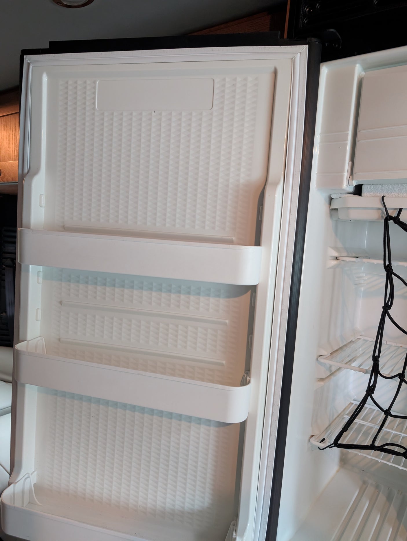 A compact rv rental refrigerator with an open door, showcasing door shelves and main compartment with a cargo net.