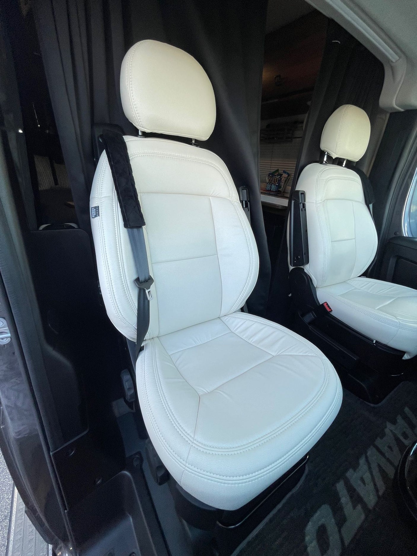 Cream-colored front seats of an RV rental camper van, likely a Winnebago Travato, with black privacy curtains behind them.