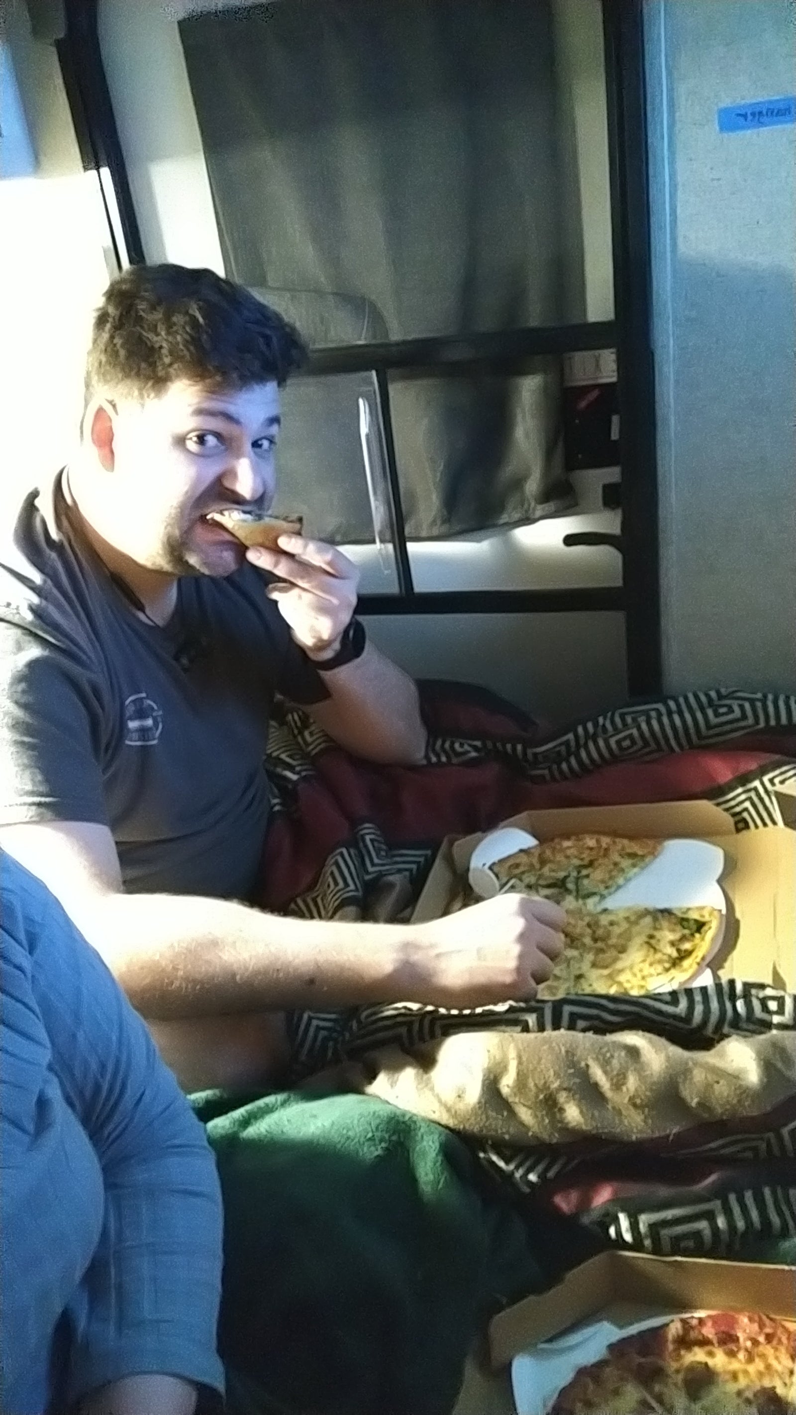 Man enjoying pizza while relaxing on a bunk bed inside an RV rental.
