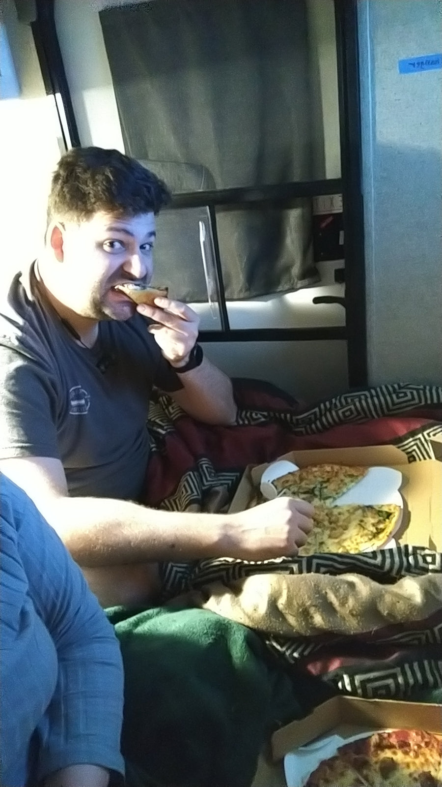 Man enjoying pizza while relaxing on a bunk bed inside an RV rental.