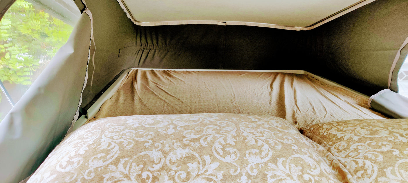 Cozy RV rental interior showing a comfortable bed with patterned pillows, bedding, and the pop-top roof, offering a nature view.