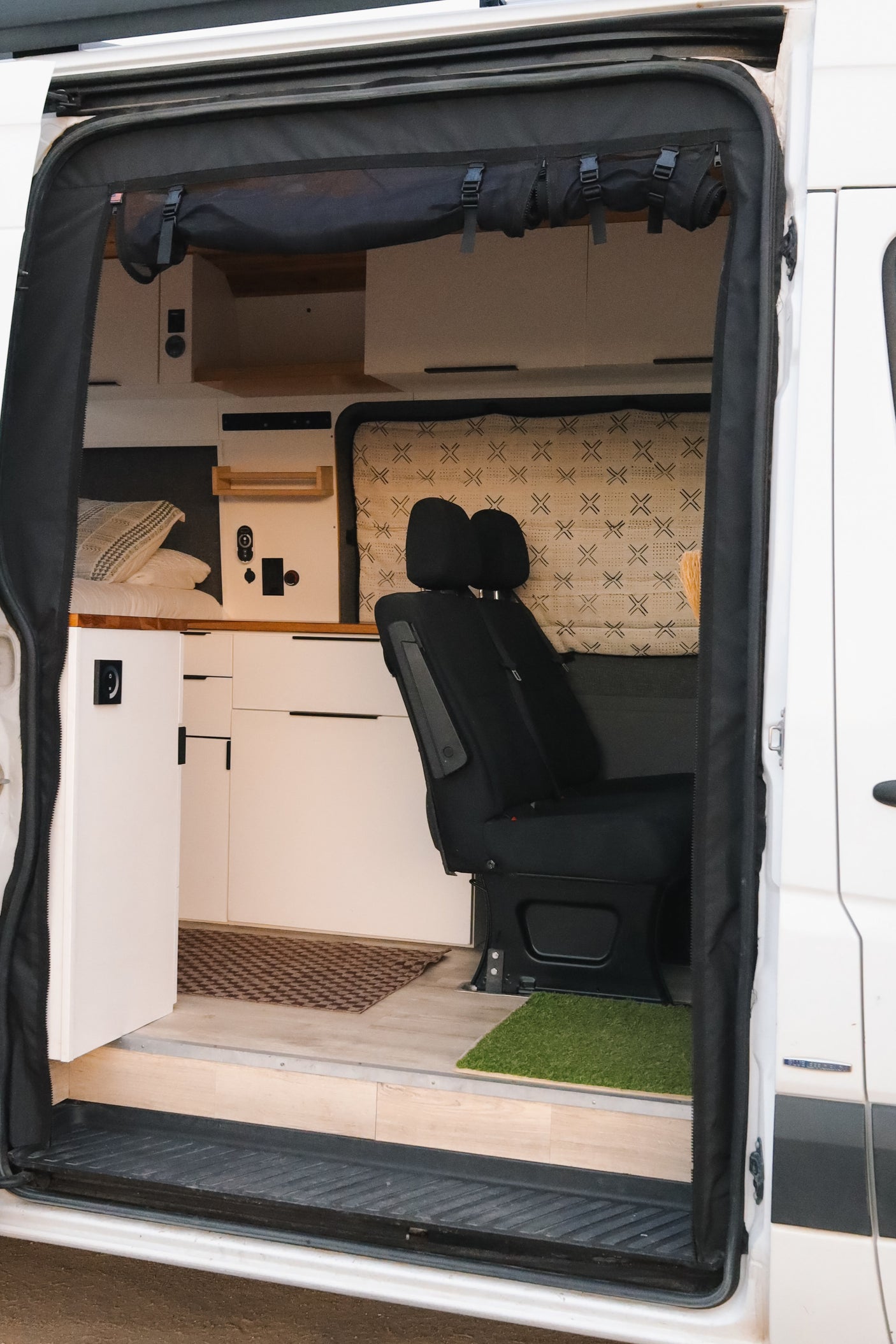 Modern rv rental camper van interior: bed, white cabinets, control panel, seating, and privacy screen.