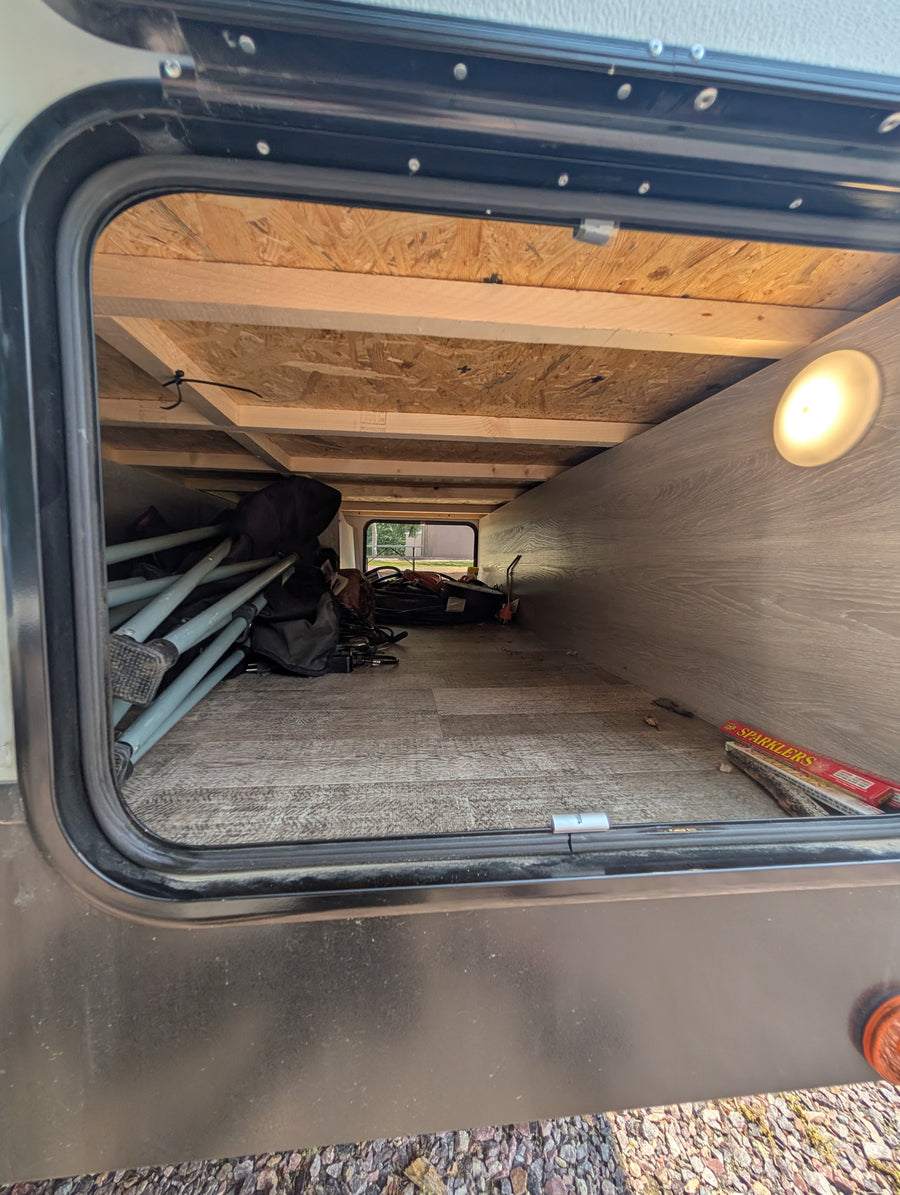 Inside an RV rental's spacious pass-through basement storage, containing folded camping chairs, bags, and a box of sparklers.