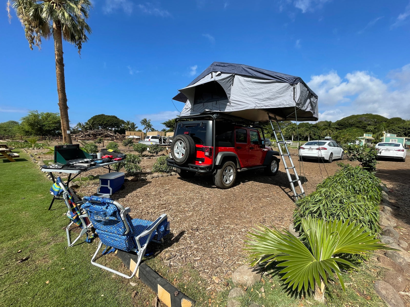 A red Jeep with a deployed rooftop tent and camp setup at a lush site. Ideal rv rental for outdoor adventures & camping!