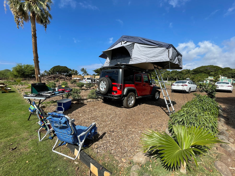 A red Jeep with a deployed rooftop tent and camp setup at a lush site. Ideal rv rental for outdoor adventures & camping!