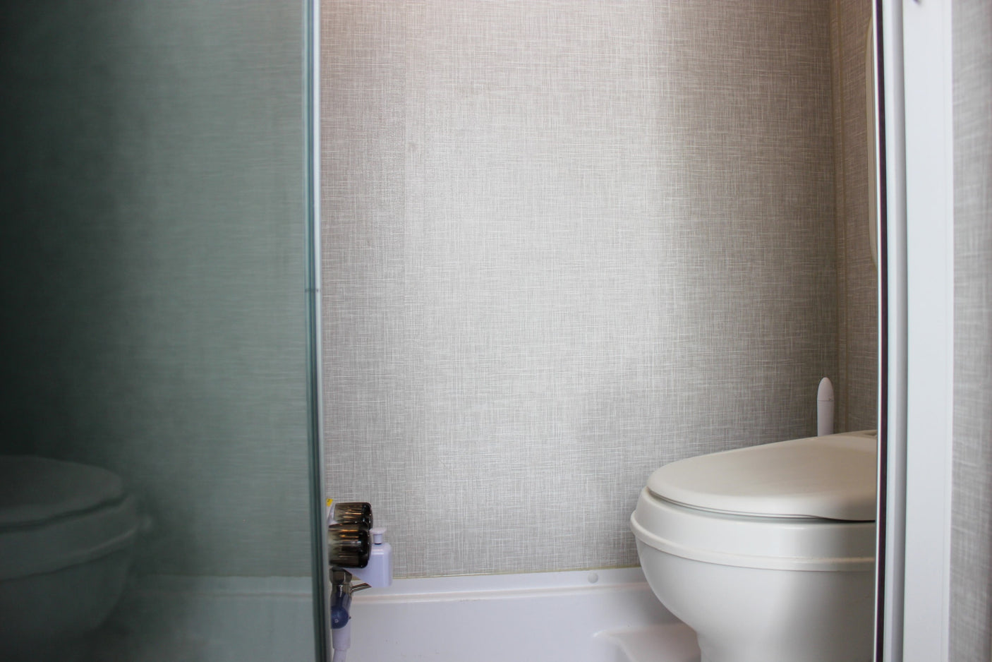 RV rental bathroom features a white toilet, textured walls, and a view through a translucent shower partition.