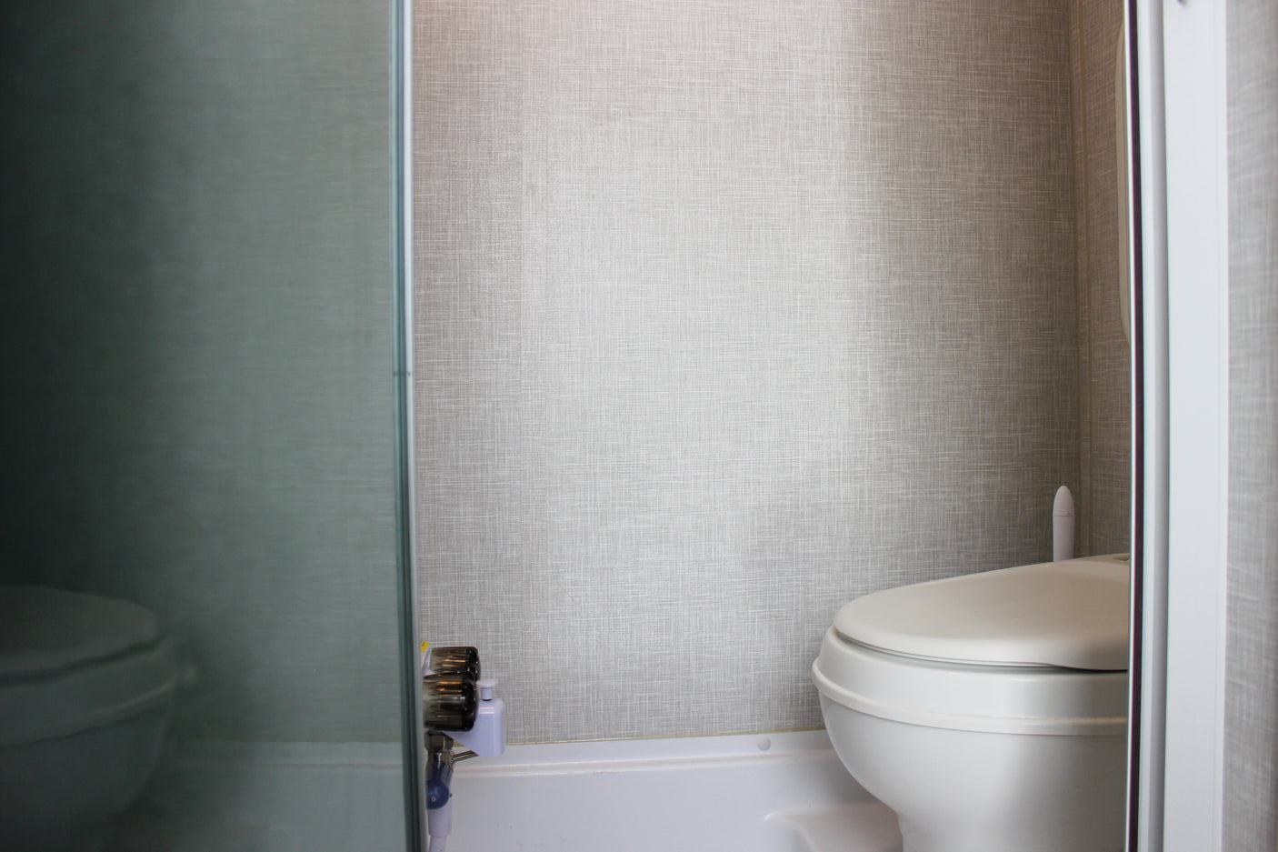 RV rental bathroom features a white toilet, textured walls, and a view through a translucent shower partition.