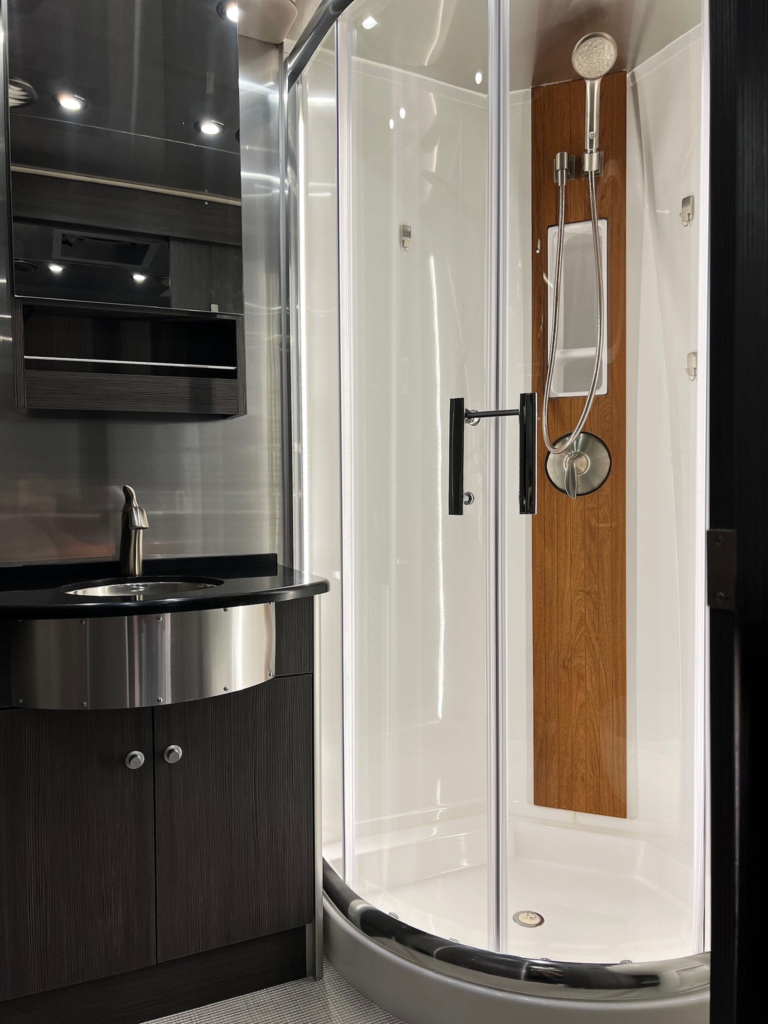 Modern RV rental bathroom: a sleek vanity with sink, clear glass shower, and wood accent panel. Compact, stylish, and ready for travel.