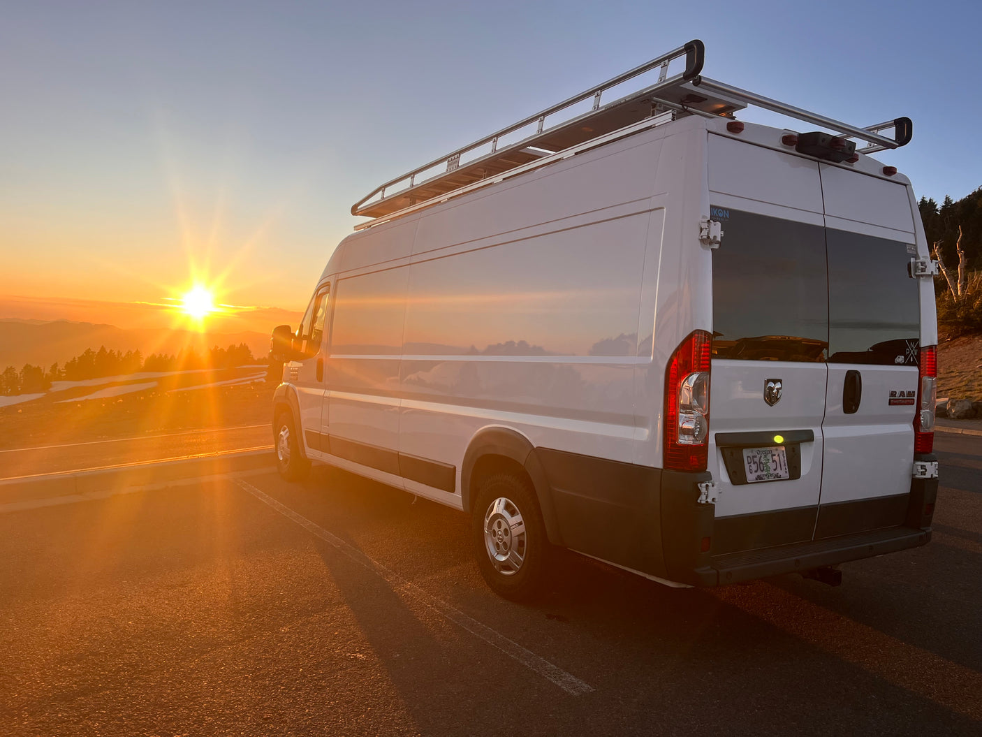White RV rental van parked at a mountain overlook under a stunning orange sunset, perfect for a road trip adventure.