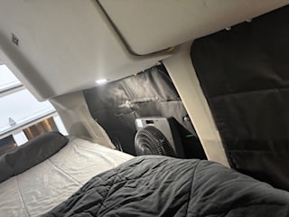 RV rental sleeping area featuring a cozy bed, privacy screens, and a fan for comfort. Perfect for road trips!