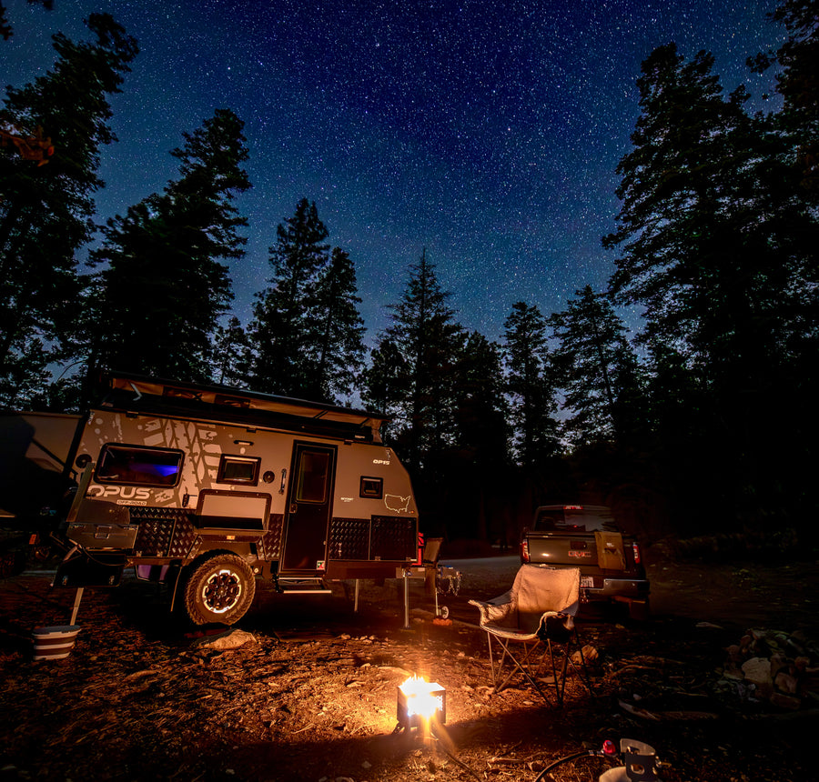 Stargazing awaits! An Opus off-road camper (RV rental) illuminates a forest campsite under a dazzling starry sky with a campfire.|Cozy rv rental campsite at dusk. Opus OP15 pop-up camper featuring an illuminated awning