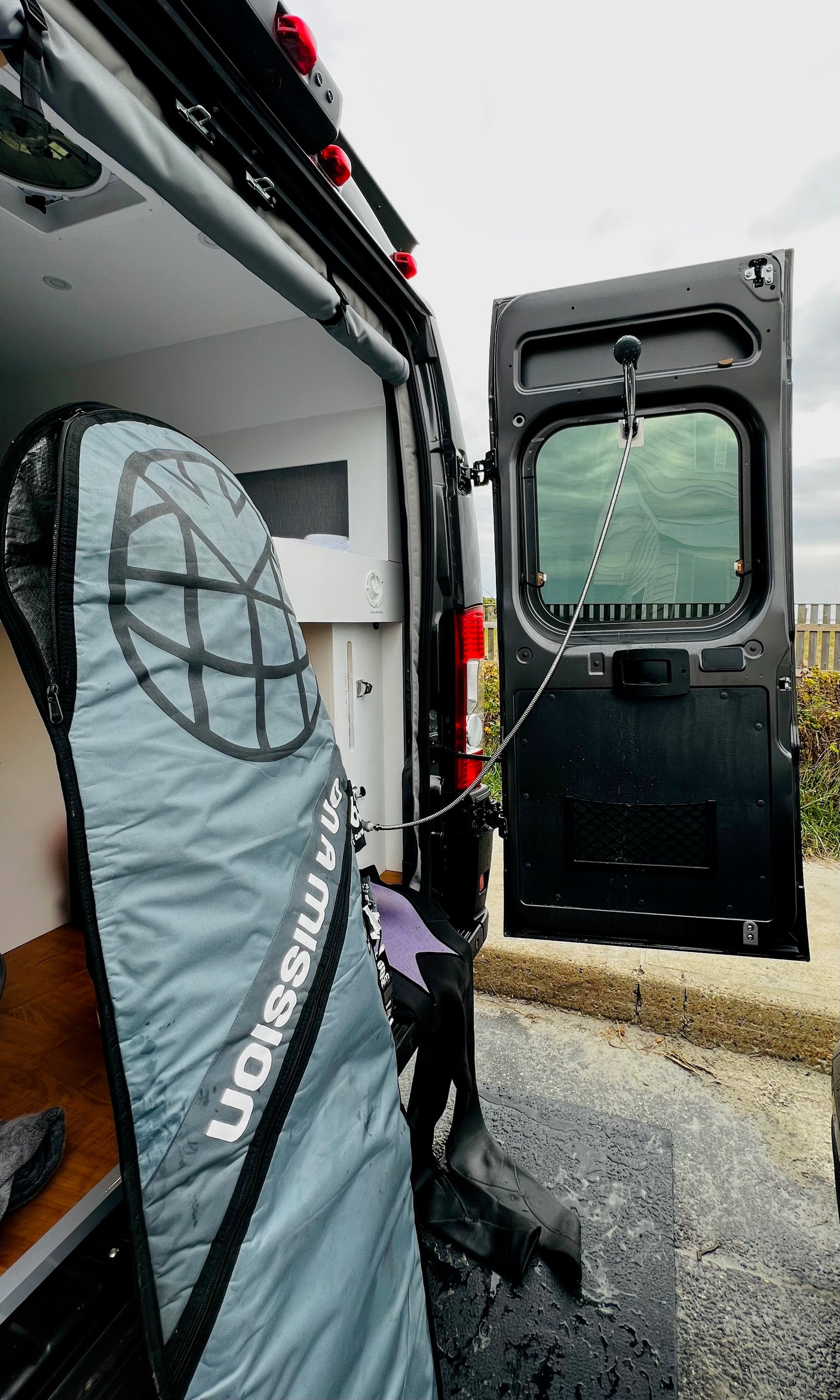 RV rental with open rear doors, revealing a surf board bag, wetsuit & an outdoor shower for post-activity cleanups.