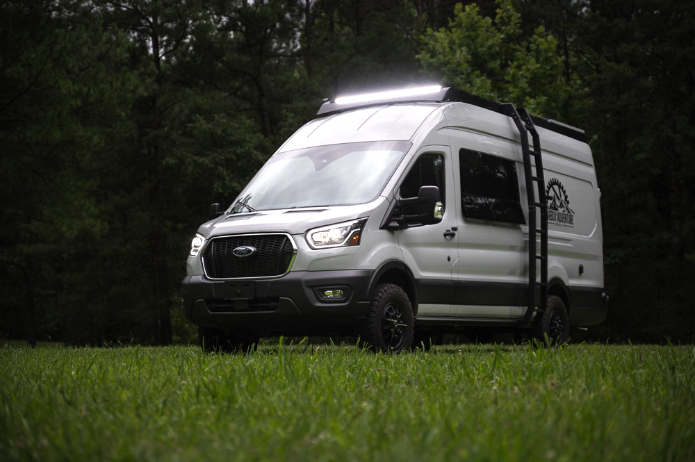 White Ford Transit camper van with bright roof lights & off-road tires, parked on grass. Ideal for your next rv rental adventure.