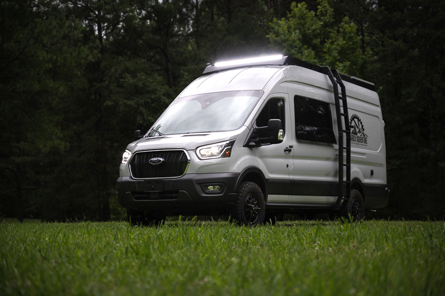 White Ford Transit camper van with bright roof lights & off-road tires, parked on grass. Ideal for your next rv rental adventure.