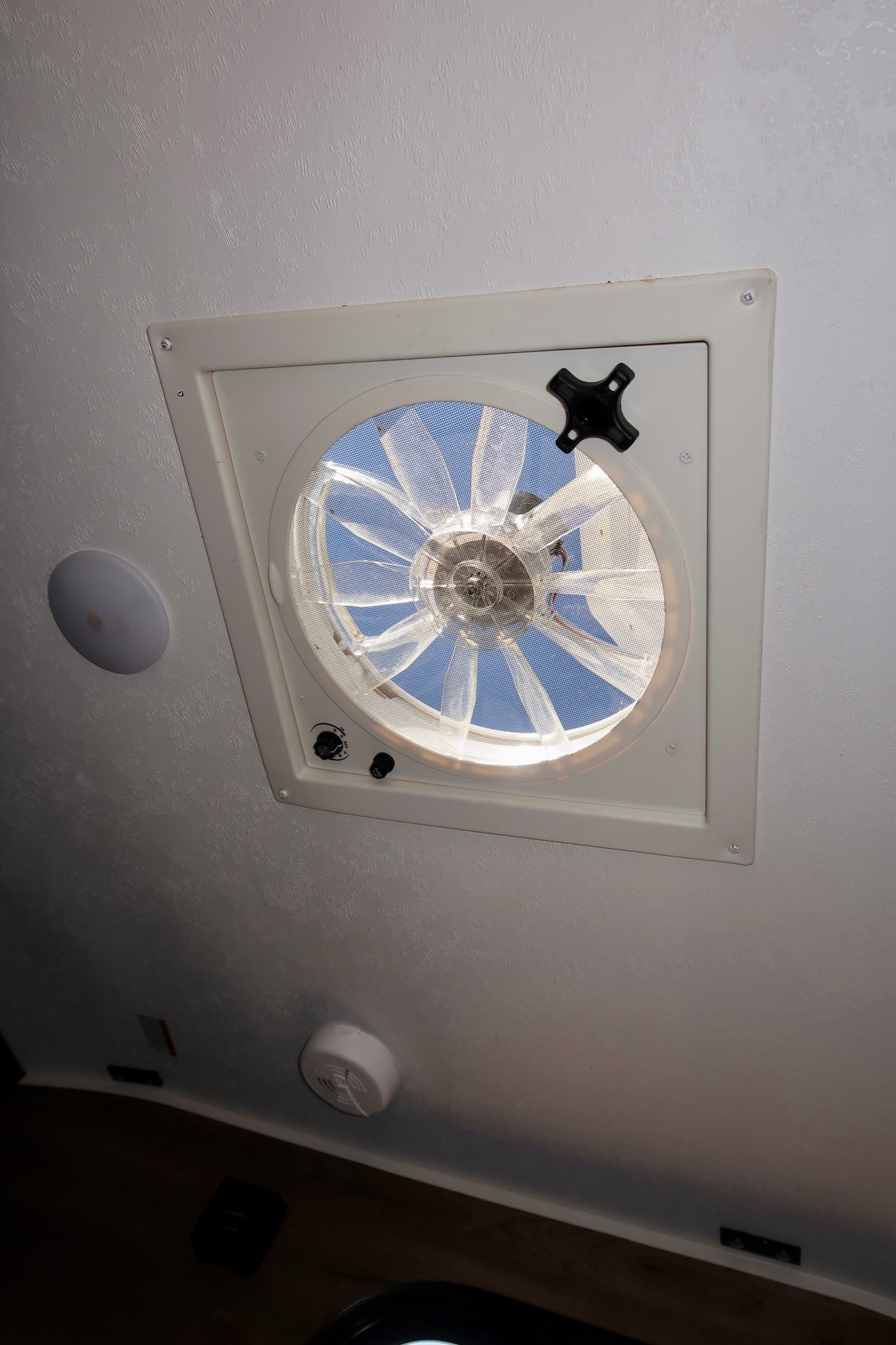RV rental ceiling: a white vent fan with a screen open to the blue sky, offering fresh air for travel.