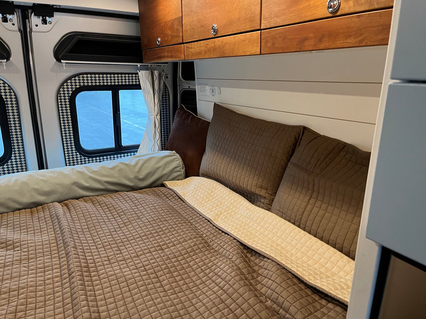 Cozy RV rental bedroom with brown quilted bedding, bolster, wooden cabinets, and white shiplap wall.