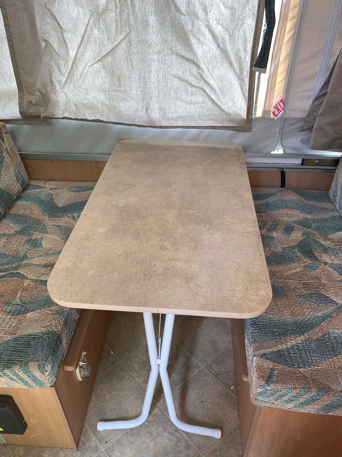 This RV rental's dinette features a removable table between two patterned bench seats, under canvas pop-up walls.