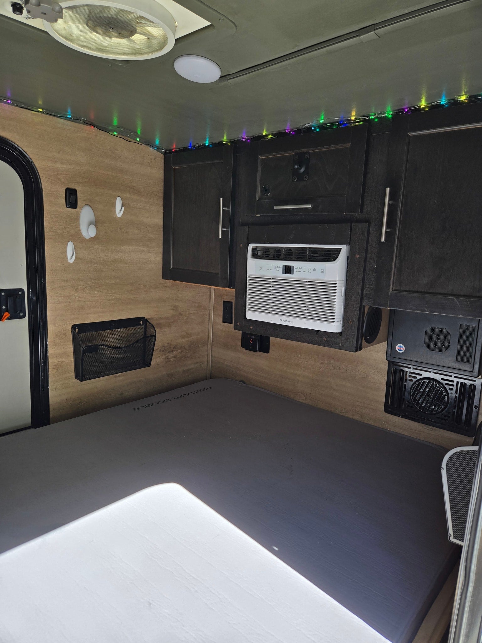 Inside a comfortable rv rental: a bed, Frigidaire AC, dark cabinets, ceiling fan, and string lights create a functional space.