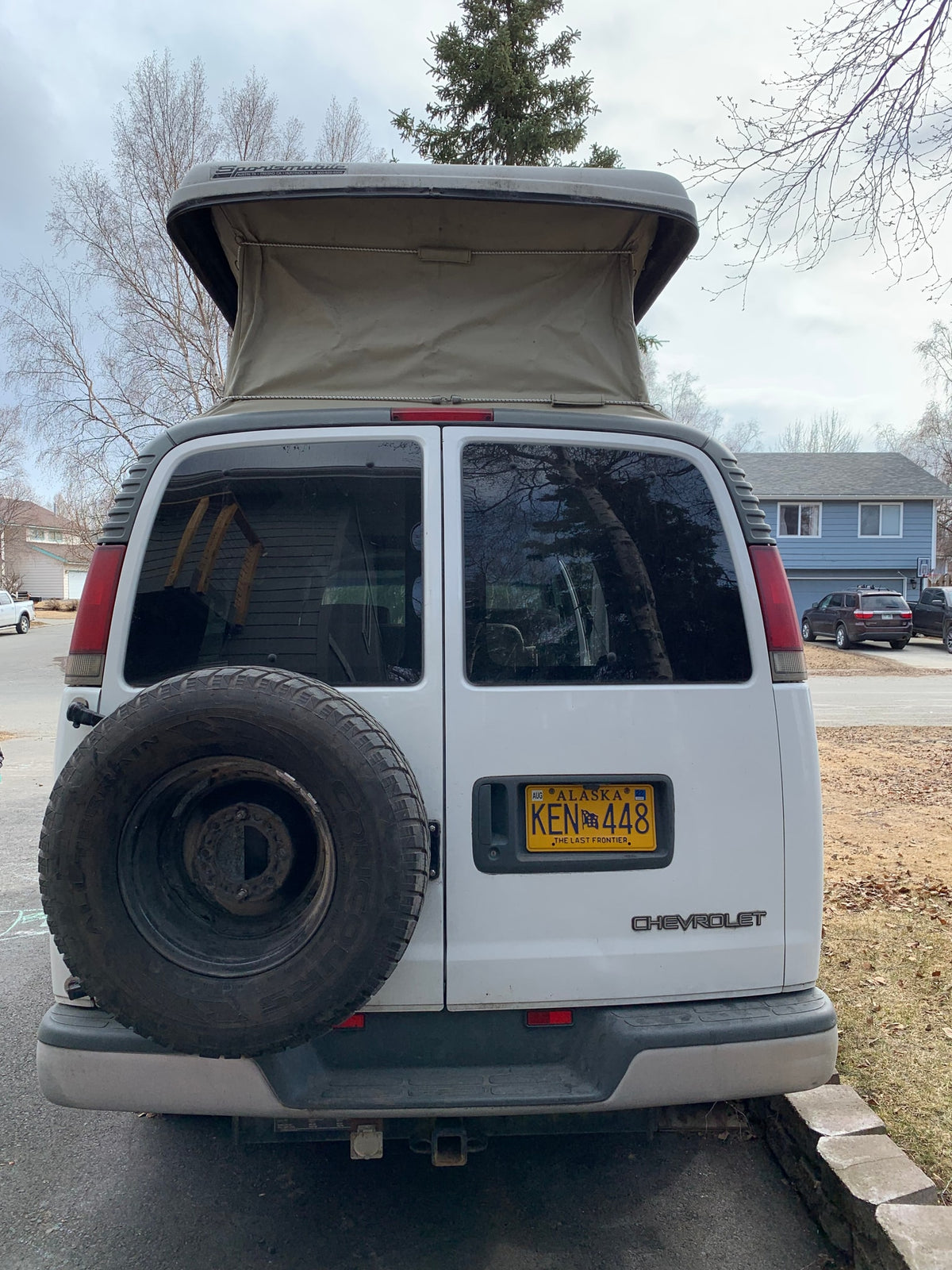 Rear view of a white Chevrolet Sportmobile pop-top camper van, an RV rental, with a spare tire and Alaska license plate. — photo 13