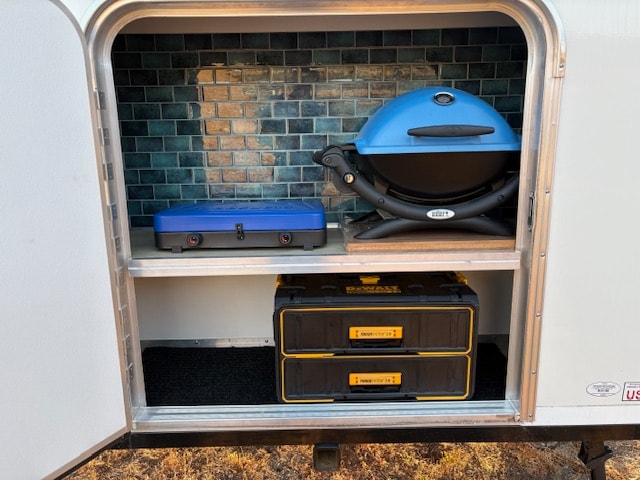 & storage net for camping.|RV rental jack securely deployed on dry ground. The black metal stabilizer leg features adjustment holes for precise leveling.|RV rental adventure: Compact outdoor kitchen with blue portable grill — photo 4