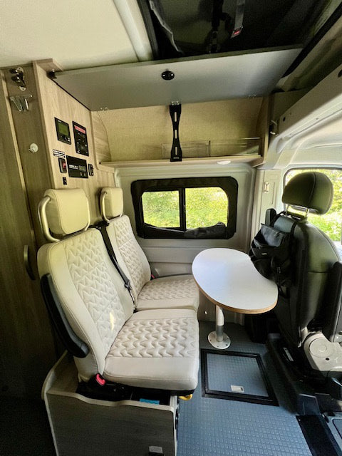 Inside a modern RV rental: light seating, flexible table, and wall controls in this compact camper van.